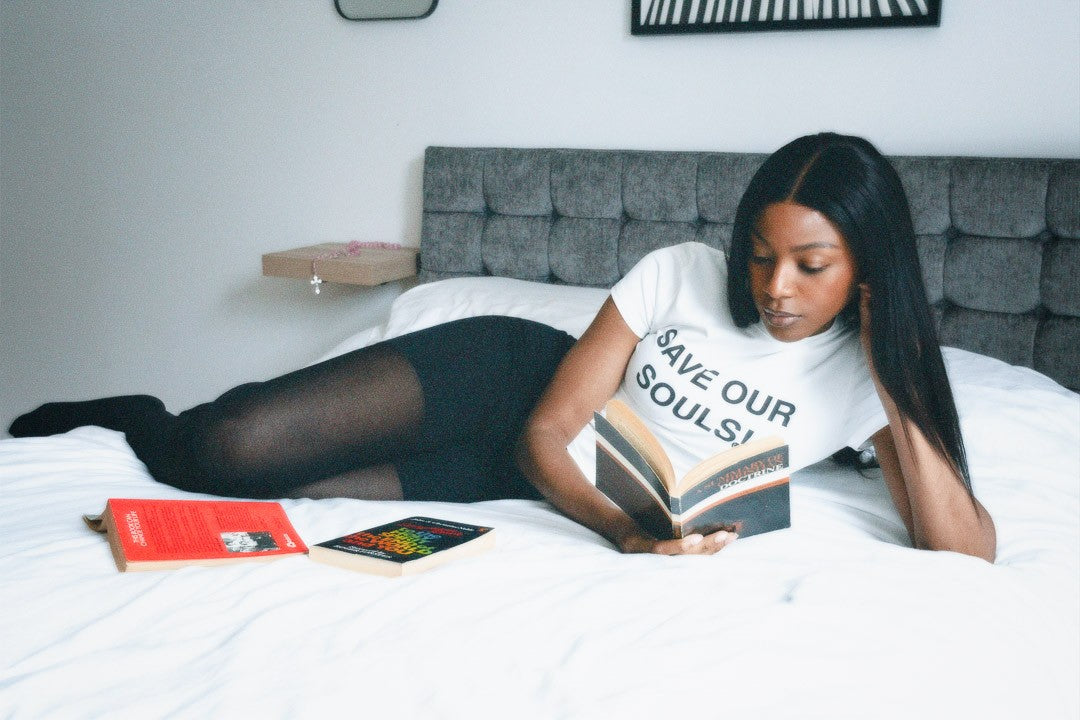 Model reclining on a bed and reading in a white SOS tee.