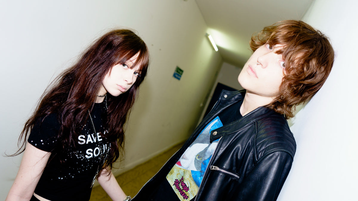 Two models posing in an indoor corridor, one wearing a black SOS top.