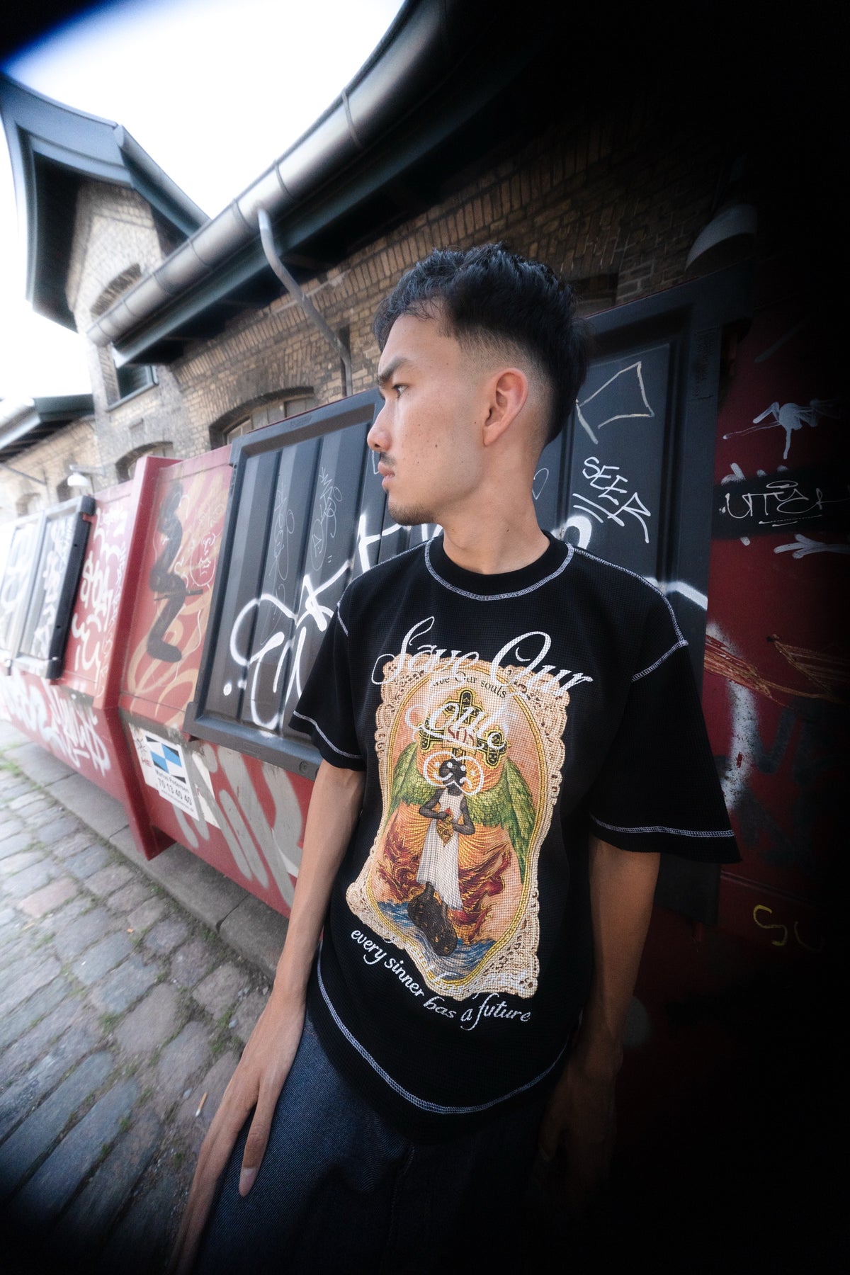 Model wearing a black Angel graphic T-shirt in a graffiti-lined alley.