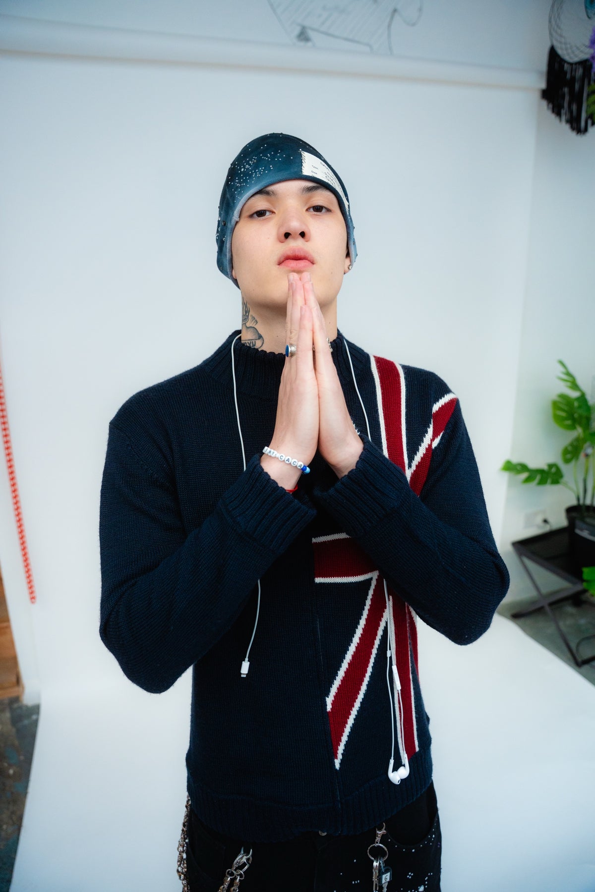 Model wearing a blue-grey rhinestone beanie and dark patterned jumper with hands together.