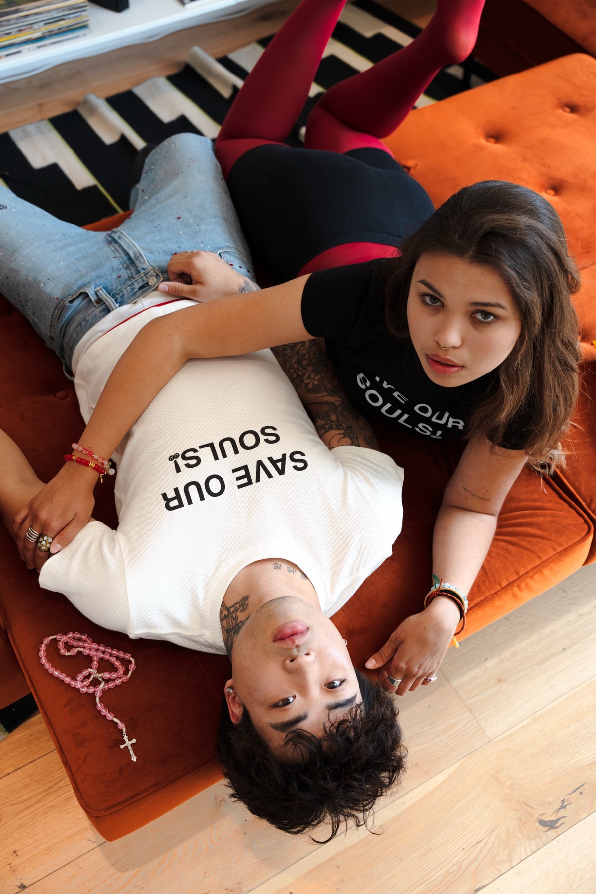 Two models wearing black and white SAVE OUR SOULS crop T-shirts on an orange chair.