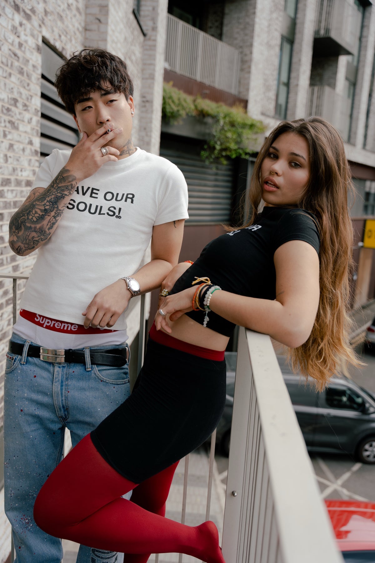 Portrait of two models wearing black and white SAVE OUR SOULS crop T-shirts on a balcony.