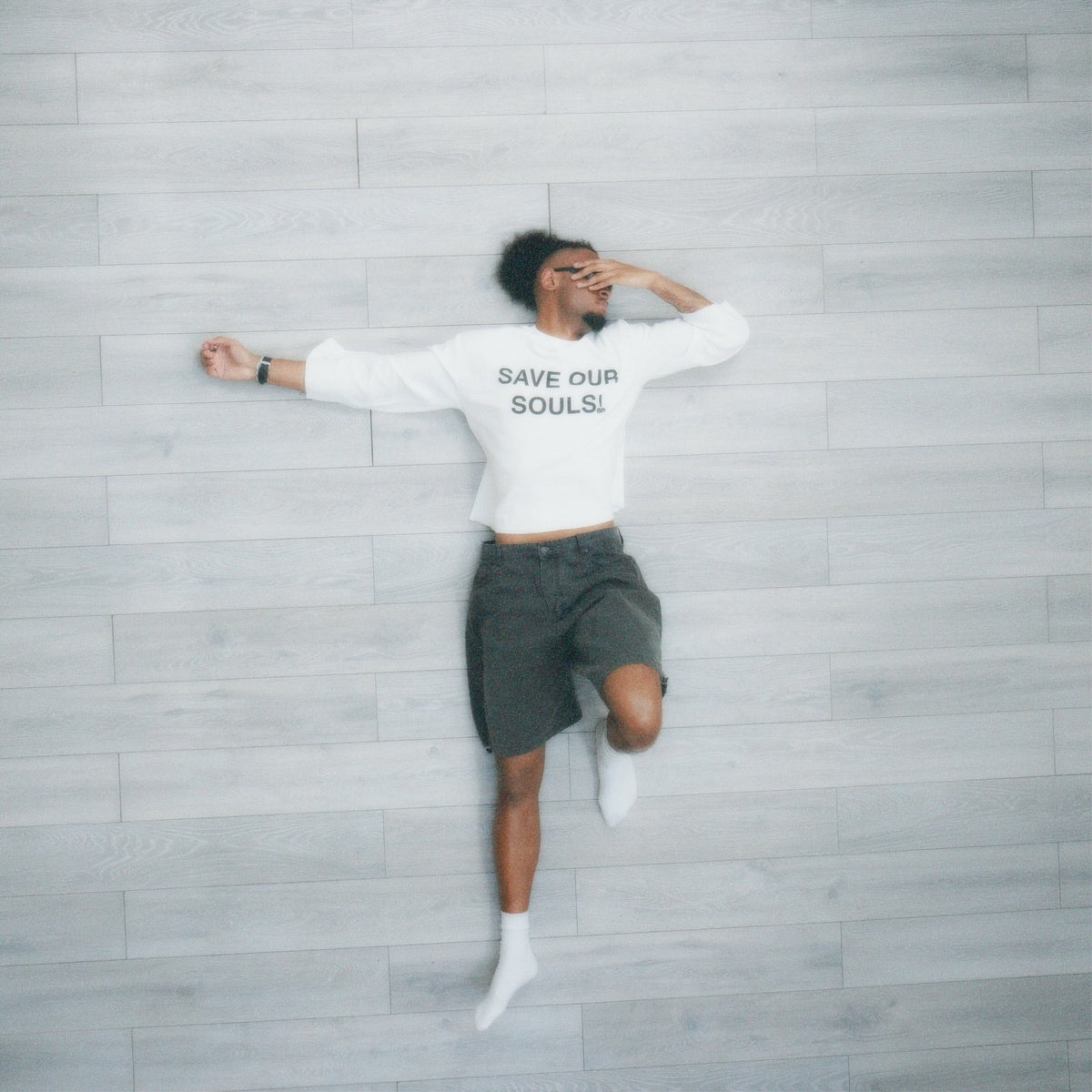Model wearing a white SAVE OUR SOULS top against a pale wall with one leg raised.