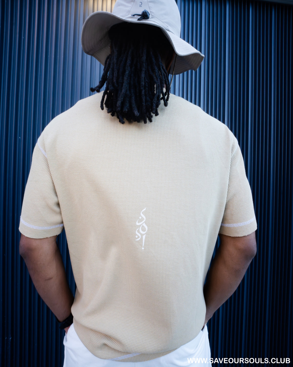 Campaign back-view photograph of a beige T-shirt with a small white SOS emblem.